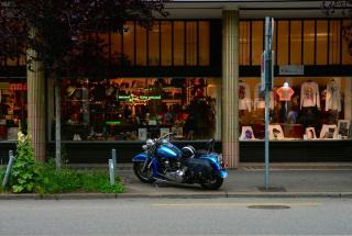 Moto à l'arrêt le long d'un trottoir, casque posé sur la selle
